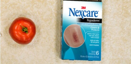 A box of Nexcare™ Tegaderm™ Dressings beside a tomato.
