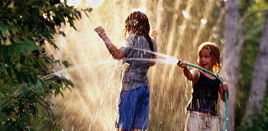 A young girl who is spraying another girl with a hose in a backyard.
