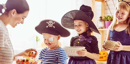 Trois enfants sont costumés et font la file pour recevoir des bonbons d’une femme pendant l’Halloween. L’enfant à l’avant, costumé en pirate, a un Couvre-œil pour peau sensible Nexcare(MC) sur son œil gauche.
