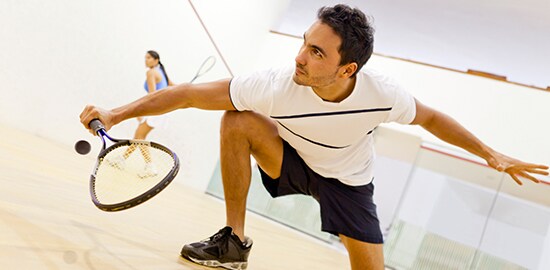 A man who is playing squash against a woman in an indoor squash court.
