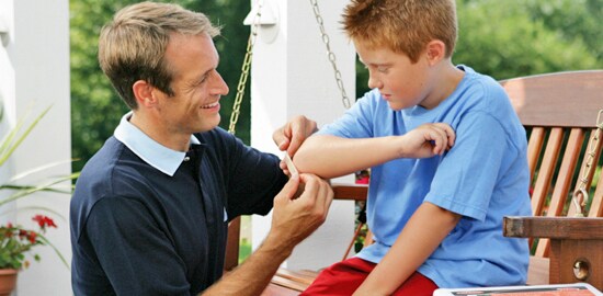 A father putting a Nexcare™ Bandage on his son's elbow.

