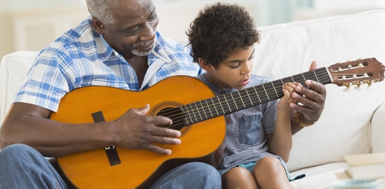 Un homme apprend à son petit-fils à jouer de la guitare.
