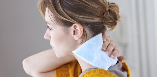 A woman applying a Nexcare™ Cold Pack to the back of her neck.
