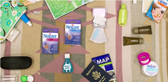 A bedspread with assorted travel items, a passport, and various first-aid and Nexcare™Brand  items.
