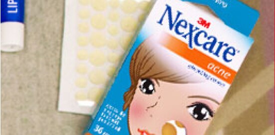 Une boîte de Timbres absorbants pour acné Nexcare(MC) sur un couvre-lit.
