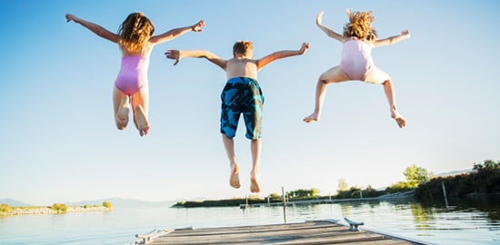 Trois enfants sautent d’un quai dans un lac.
