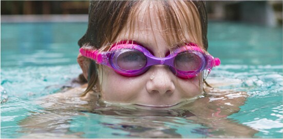 A young girl swimming a pool, wearing goggles. Her mouth is under the water.
