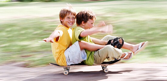 Deux jeunes garçons sont assis sur une planche à roulettes qui roule vers le bas un trottoir.
