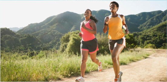 Two women running on a dirt trail. There are tree covered hills in the background.
