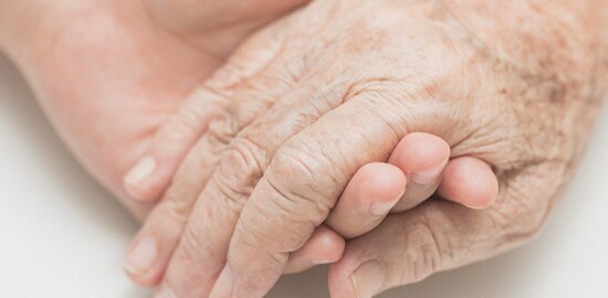 An elderly woman's hand grasping a younger person's hand.
