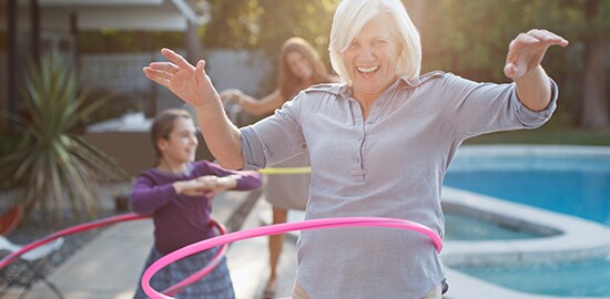 An older lady hoola hooping beside a pool. Her daughter and grand-daughter are in the background.
